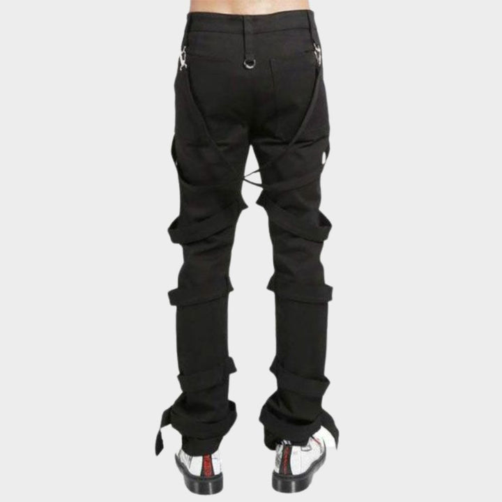 Black gothic tripp pants laid flat, displaying the pitch-black fabric, removable bondage straps with buckles, and four functional pockets for a customizable gothic look.